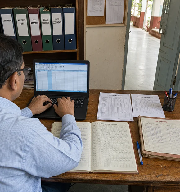 School records kept in paper registers alongside a spreadsheet